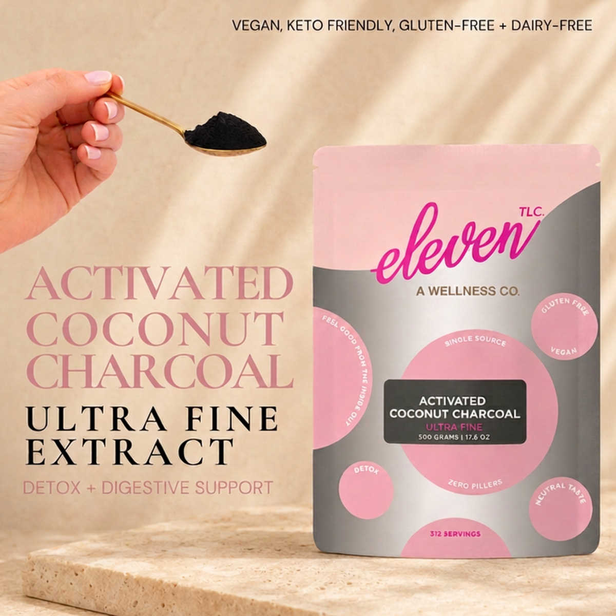 Hand holding a gold spoon of ultra-fine black activated coconut charcoal powder beside the Eleven TLC 500 g pouch on a stone ledge in warm window light.