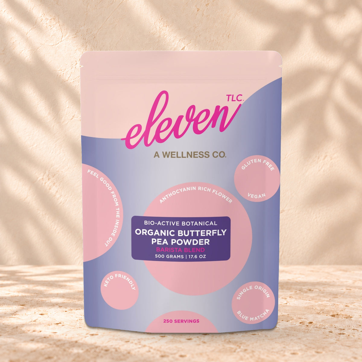Eleven TLC Butterfly Pea Flower Powder 500g stand-up pouch on travertine stone against a warm cream plaster wall, lit from the left with a soft shadow to the right.