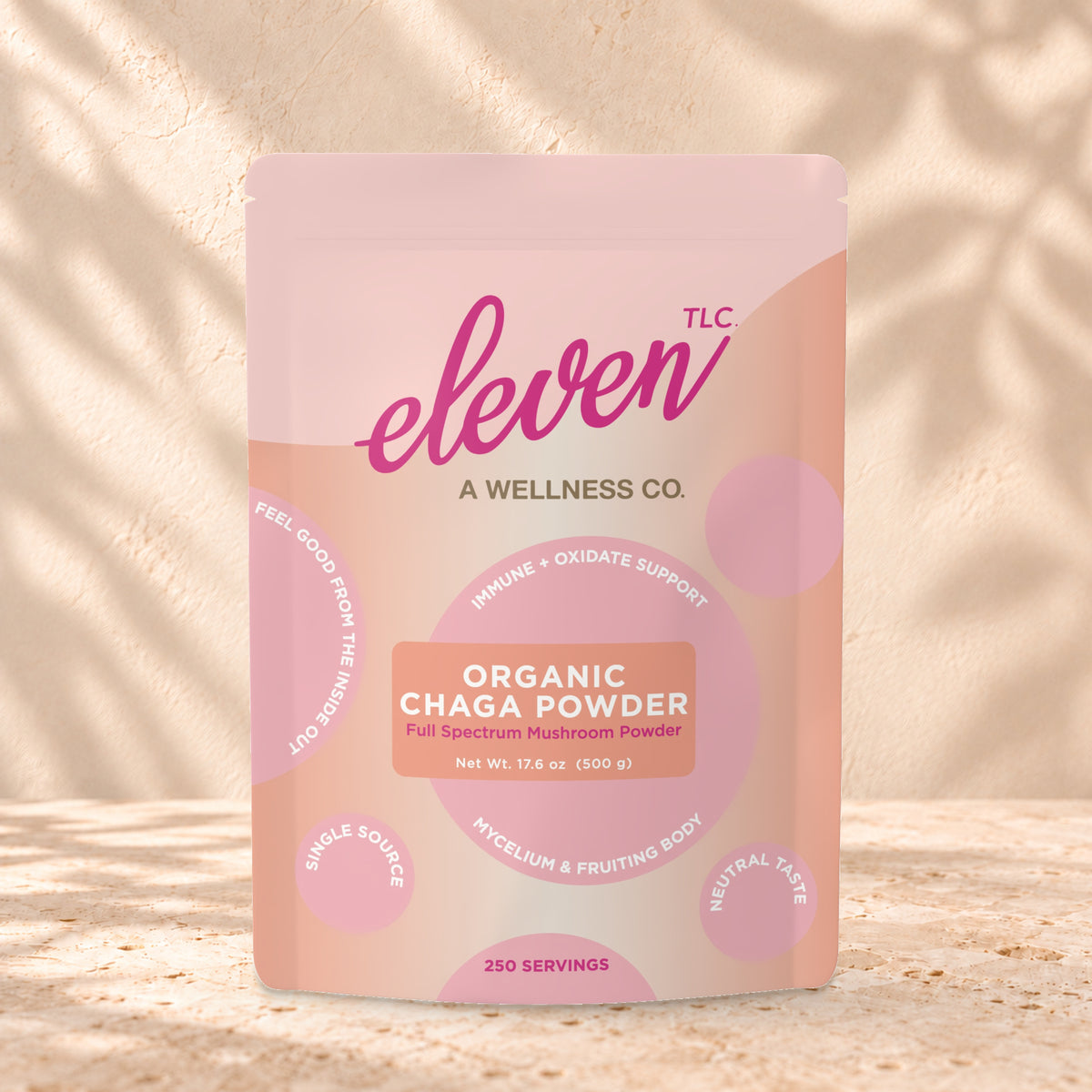 Eleven TLC Organic Chaga Mushroom Powder 500g stand-up pouch on travertine stone against a warm cream plaster wall, lit from the left with a soft shadow to the right.