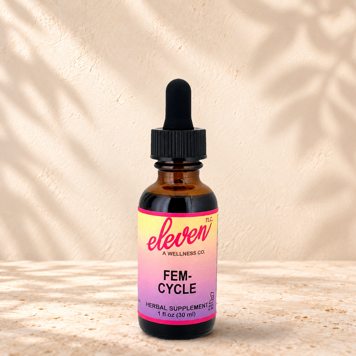Eleven TLC Fem-Cycle herbal tincture for cycle support, 1 fl oz amber dropper bottle with pink and yellow label on stone