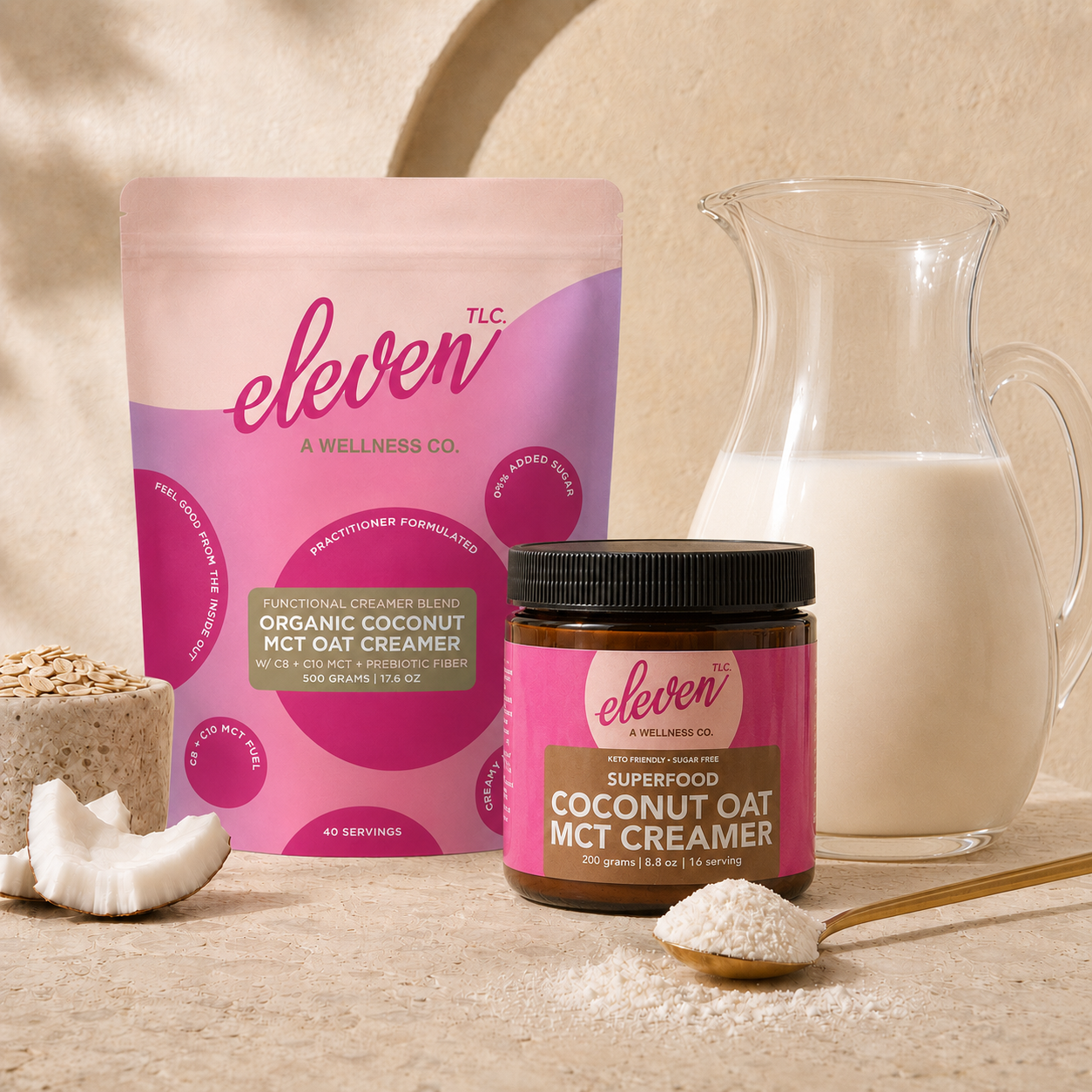 Product hero shot of Eleven TLC organic coconut oat mct creamer, featuring a 500g flexible stand-up pouch and an amber glass jar, arranged on a neutral stone surface; includes a glass carafe of prepared beverage, raw coconut chunks, and a spoonful of powdered creamer for texture context, set in warm, soft-focus studio lighting.