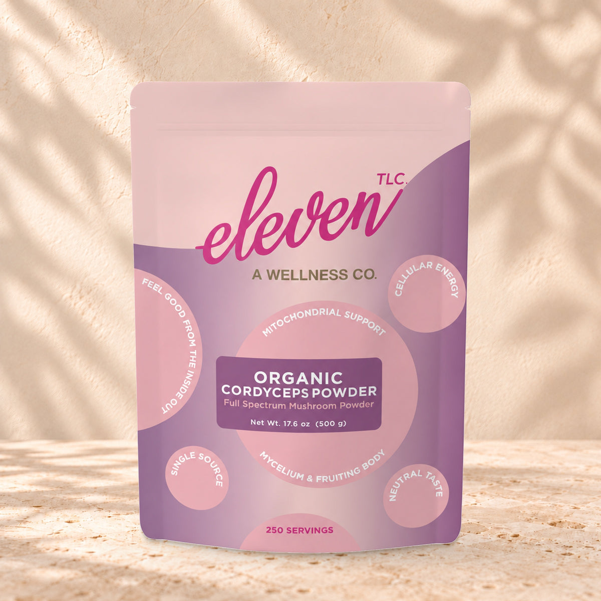Eleven TLC Organic Cordyceps Mushroom Powder 500g stand-up pouch on travertine stone against a warm cream plaster wall, lit from the left with a soft shadow to the right.