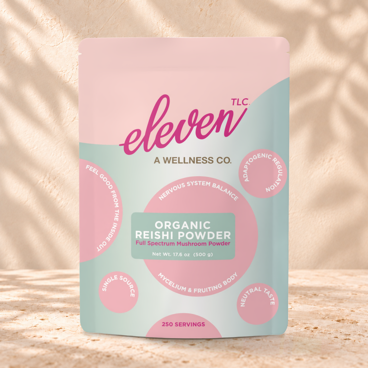 Eleven TLC Reishi 500g sage green and pink pouch standing on a travertine ledge against warm plaster, with a contact shadow beneath the base and a soft shadow to the right.