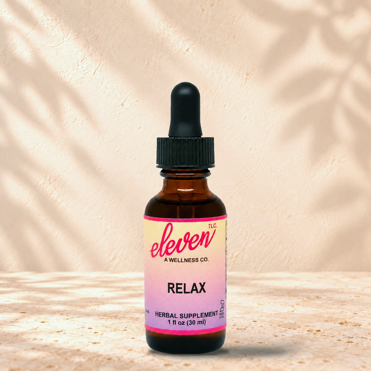 Eleven TLC Relax herbal supplement tincture in a 1 fl oz (30 ml) amber glass dropper bottle with a pink-to-lavender label, standing on a stone surface with soft leaf shadows