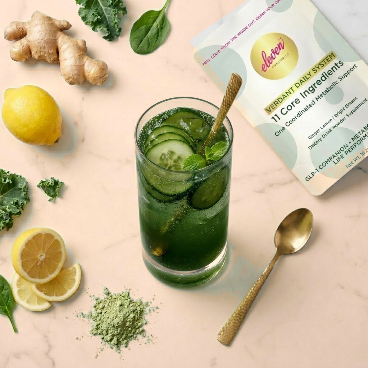 Overhead view of the Eleven TLC Verdant Daily System pouch and a green drink with cucumber, fresh ginger, lemon, kale and spinach on warm cream marble.