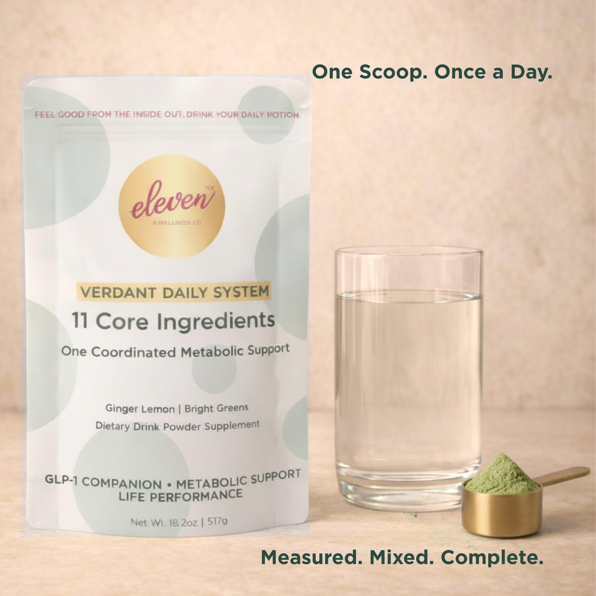 Eleven TLC Verdant Daily System pouch beside a glass of water and a gold scoop of green powder on warm sand-toned stone. One scoop, once a day.