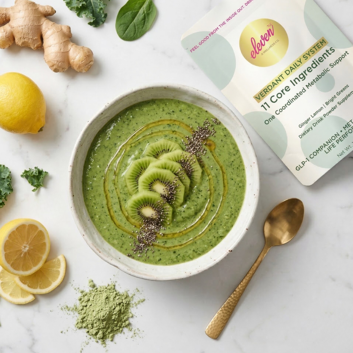 Green Verdant Daily System smoothie bowl topped with kiwi and chia seeds beside the Eleven TLC 517g pouch, lemon, ginger and a gold spoon on warm cream marble.