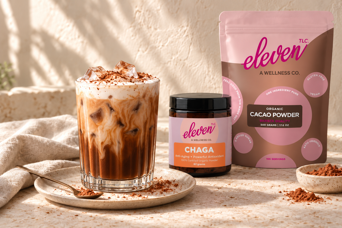 Creamy iced Chagaccino in a clear glass beside Eleven TLC Chaga 82g jar and Organic Cacao Powder 500g pouch.