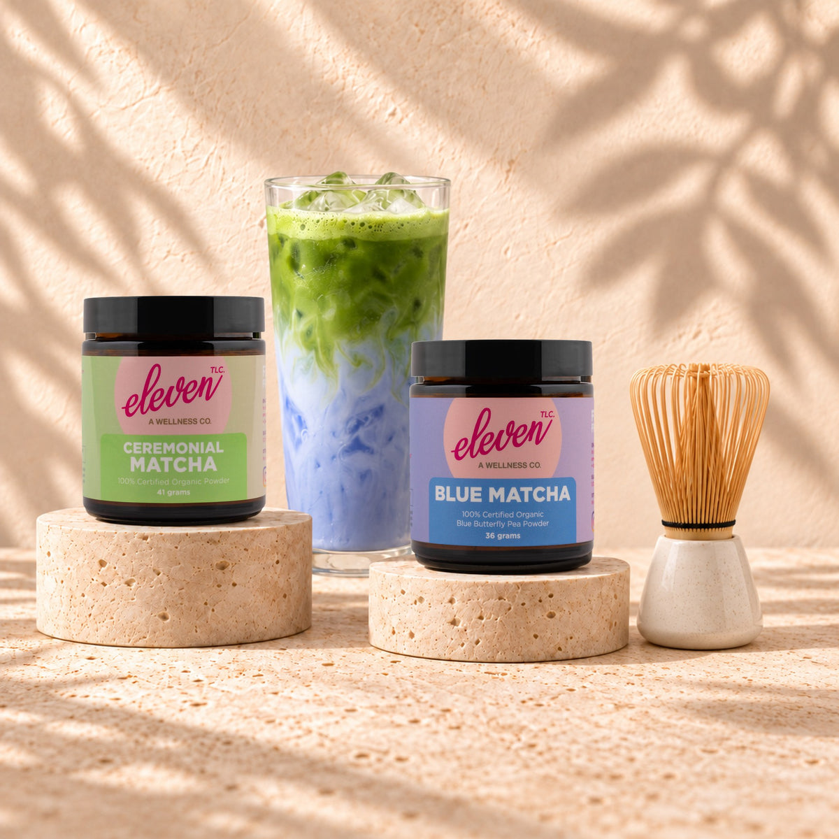 Eleven TLC Ceremonial Matcha and Blue Matcha jars with a layered iced matcha latte and bamboo whisk