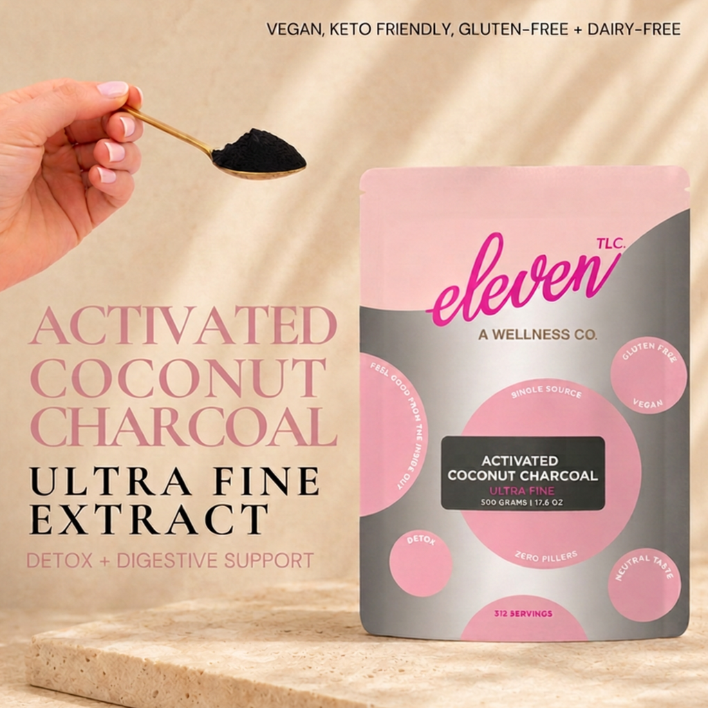 Hand holding a gold spoon of ultra-fine black activated coconut charcoal powder beside the Eleven TLC 500 g pouch on a stone ledge in warm window light.