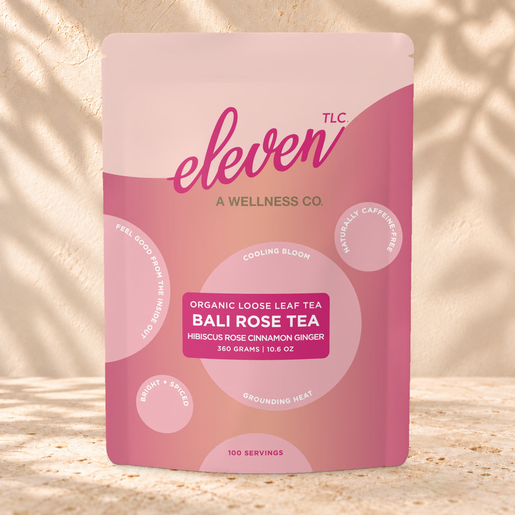 Front view of an Eleven TLC Bali Rose Tea 360g pouch on warm travertine against a cream plaster wall with botanical shadows.