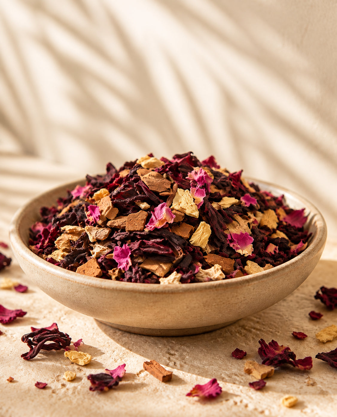 Close-up of Bali Rose loose-leaf tea with dried hibiscus, rose petals, golden cut ginger and Ceylon cinnamon in a ceramic bowl on warm cream travertine.