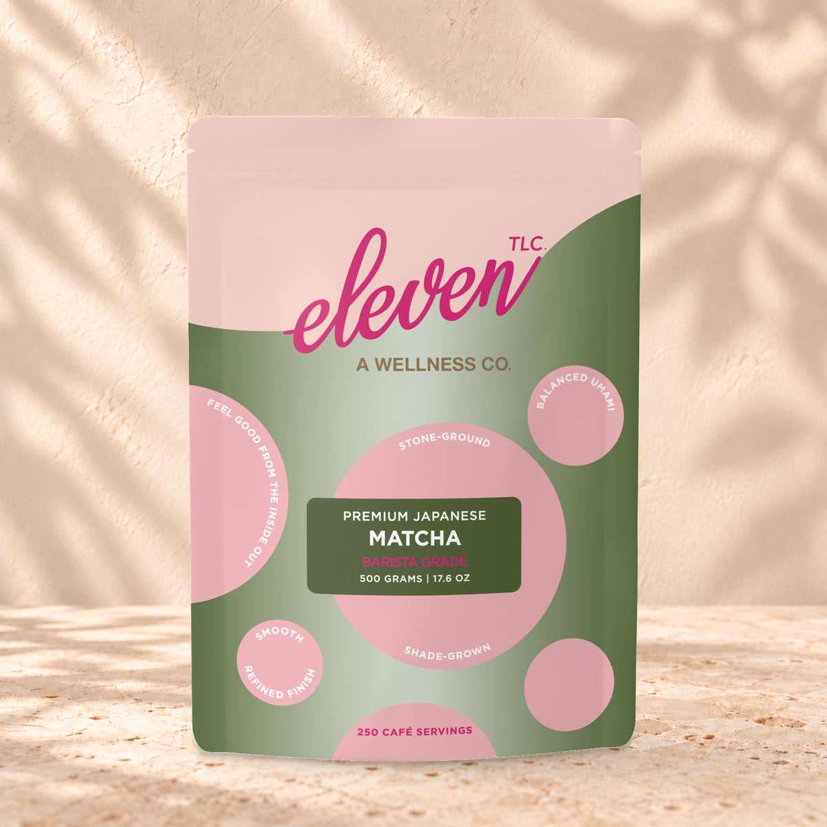 Eleven TLC Organic Barista Matcha Powder 500g stand-up pouch on travertine stone against a warm cream plaster wall, lit from the left with a soft shadow to the right.