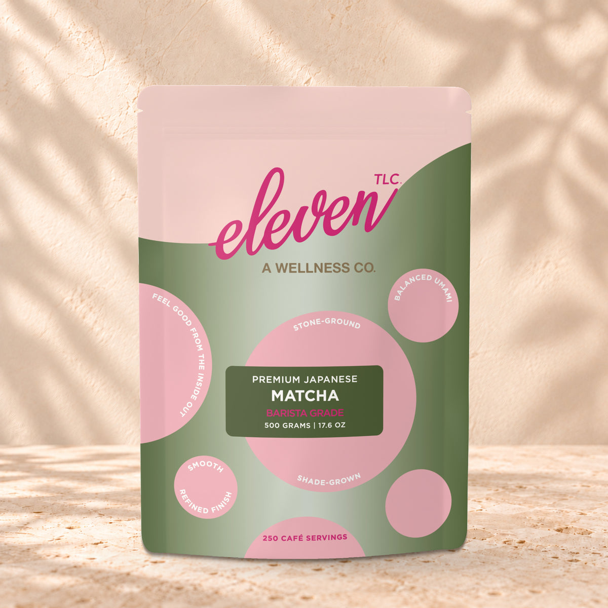 Eleven TLC Organic Barista Matcha Powder 500g stand-up pouch on travertine stone against a warm cream plaster wall, lit from the left with a soft shadow to the right.