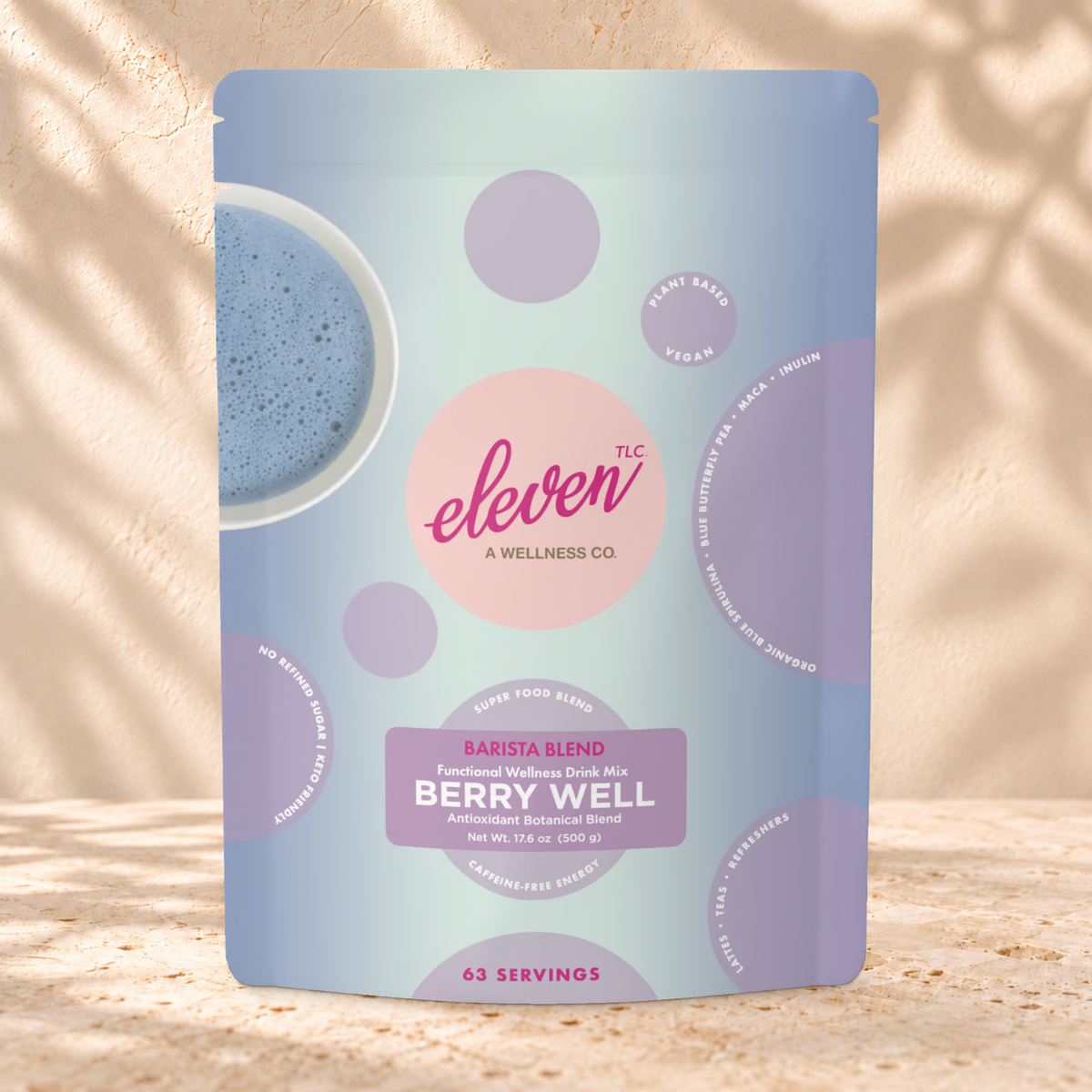 Front view of an Eleven TLC Berry Well 500g pouch on warm travertine against a cream plaster wall with botanical shadows.