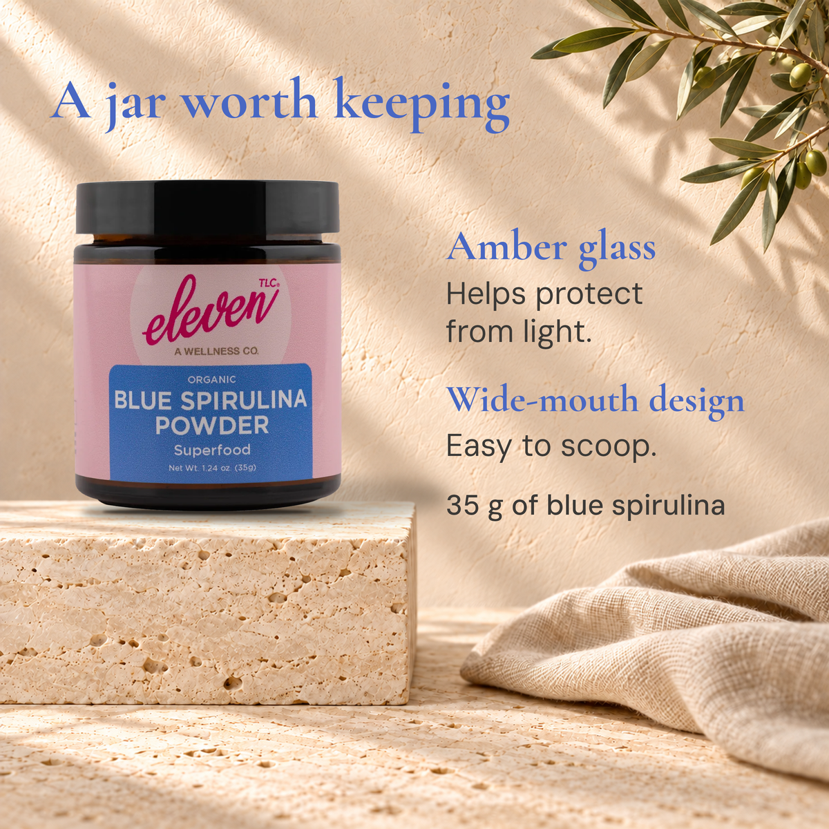 Eleven TLC Blue Spirulina Powder 35g amber-glass jar on a stone block beside linen and greenery, with packaging information.