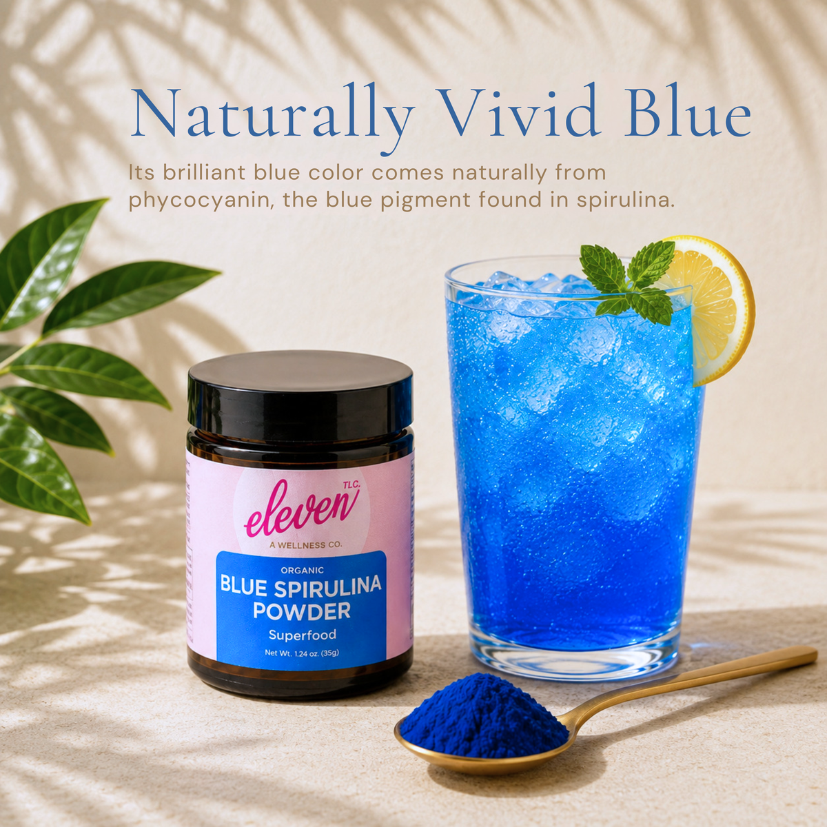 Eleven TLC blue spirulina jar and spoonful of powder beside a vivid blue iced drink garnished with lemon and mint.