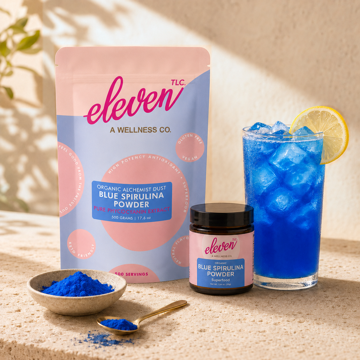 Eleven TLC 500g pouch and 35g jar beside a tall blue drink with lemon, a powder bowl and a gold spoon.