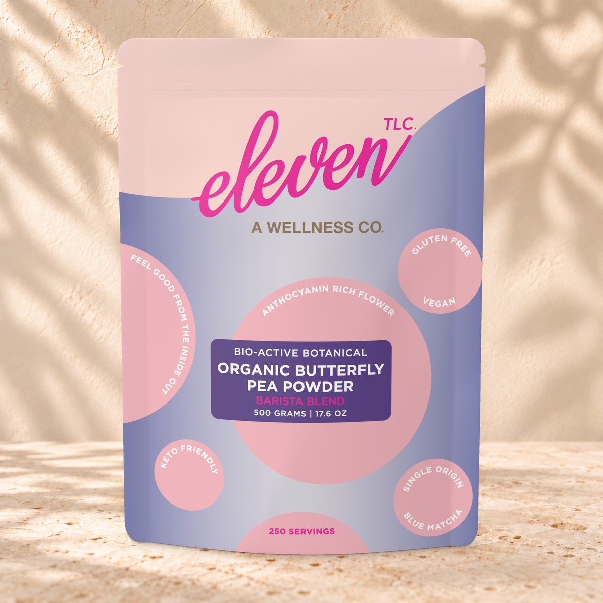 Front view of an Eleven TLC Butterfly Pea Powder 500g pouch on warm travertine against a cream plaster wall with botanical shadows.