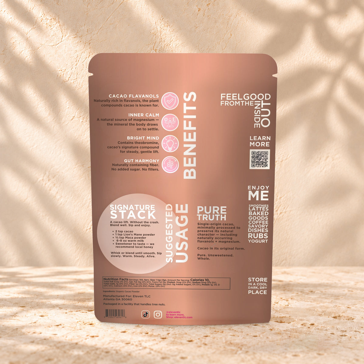 Back view of an Eleven TLC Cacao Powder 500g pouch on warm travertine against a cream plaster wall with botanical shadows.