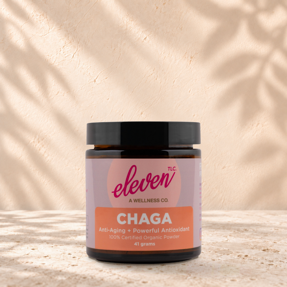 Eleven TLC Chaga 41 gram mushroom powder jar with a black lid standing on travertine against a warm plaster backdrop.