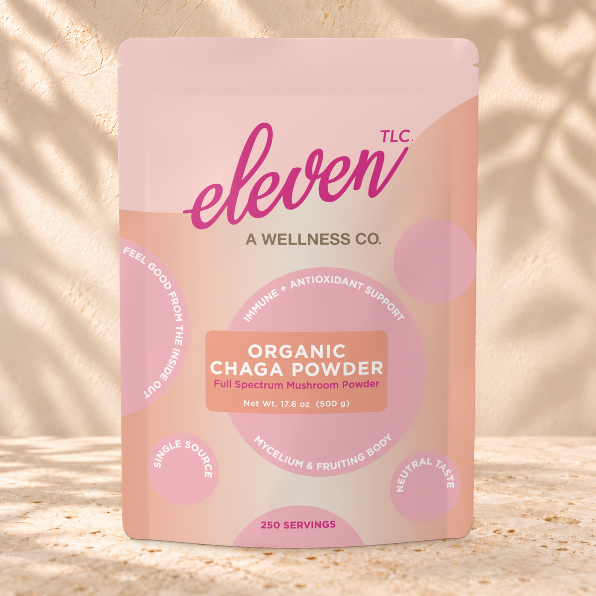 Front view of an Eleven TLC Chaga Mushroom Powder 500g pouch on warm travertine against a cream plaster wall with botanical shadows.