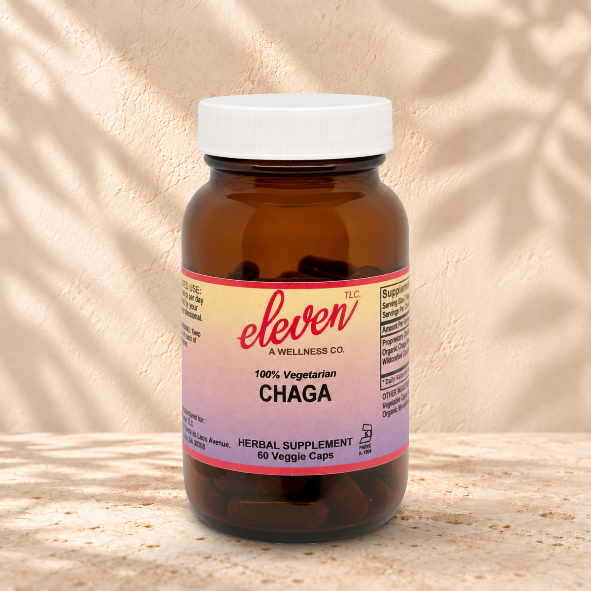 Eleven TLC Chaga 60-count capsule bottle with a white lid on warm travertine against cream plaster, with soft contact shadows.
