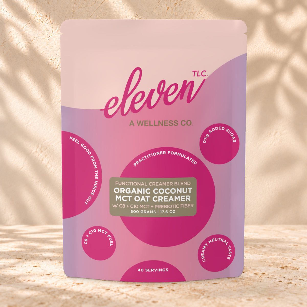 Front view of an Eleven TLC Coconut MCT Oat Creamer 500g pouch on warm travertine against a cream plaster wall with botanical shadows.