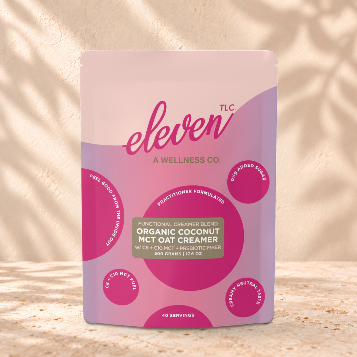 Eleven TLC Organic Coconut MCT Oat Creamer 500g stand-up pouch on travertine stone against a warm cream plaster wall, lit from the left with a soft shadow to the right.