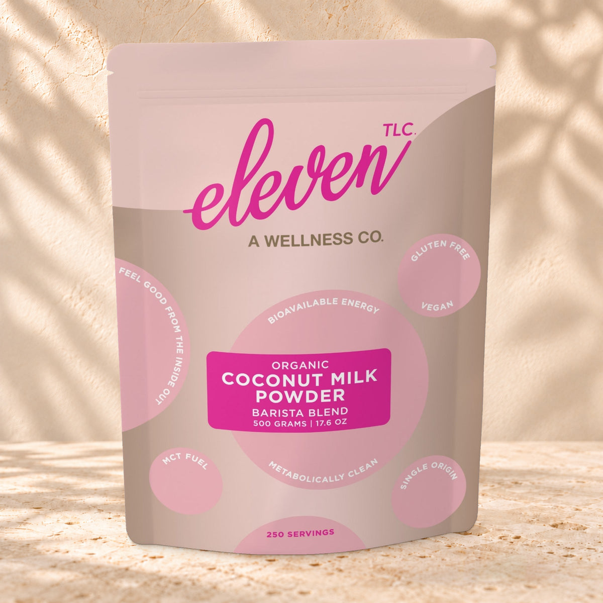Front view of an Eleven TLC Coconut Milk Powder 500g pouch on warm travertine against a cream plaster wall with botanical shadows.