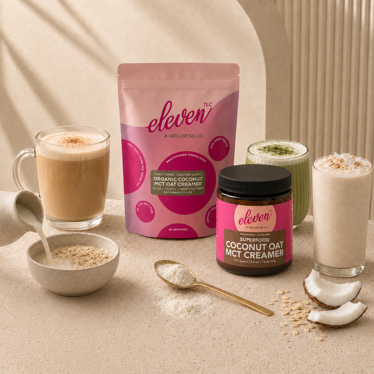 Lifestyle composition showcasing the Eleven TLC coconut oat mct creamer ecosystem, including a 500g flexible stand-up pouch and an amber glass jar, accompanied by two glass mugs of prepared beverages; one mug displays a clear, creamy liquid, while the other features a froth-topped matcha drink, staged on a neutral limestone surface with raw coconut and oat accents in warm, soft-focus natural lighting.