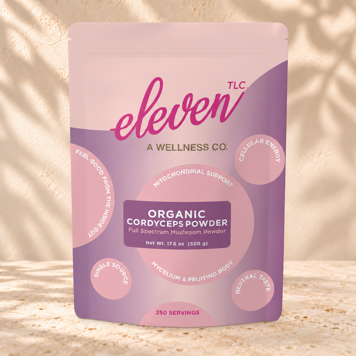 Front view of an Eleven TLC Cordyceps Mushroom Powder 500g pouch on warm travertine against a cream plaster wall with botanical shadows.