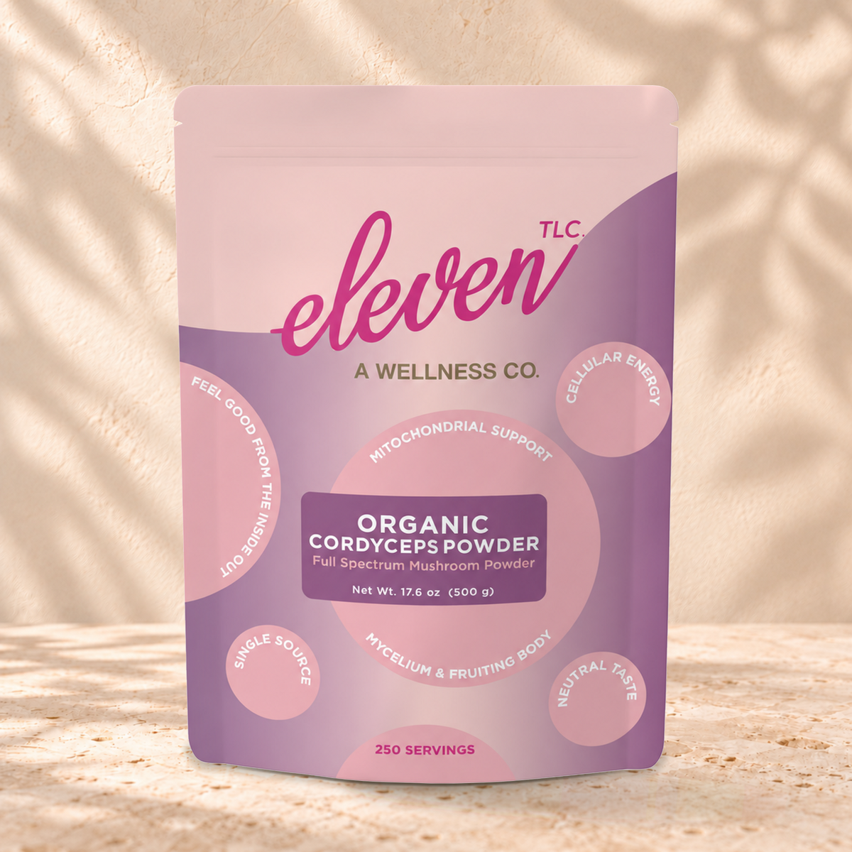 Eleven TLC Cordyceps Mushroom Powder 500g purple and pink pouch standing on a travertine ledge against warm plaster, with a contact shadow beneath the base and a soft shadow to the right.