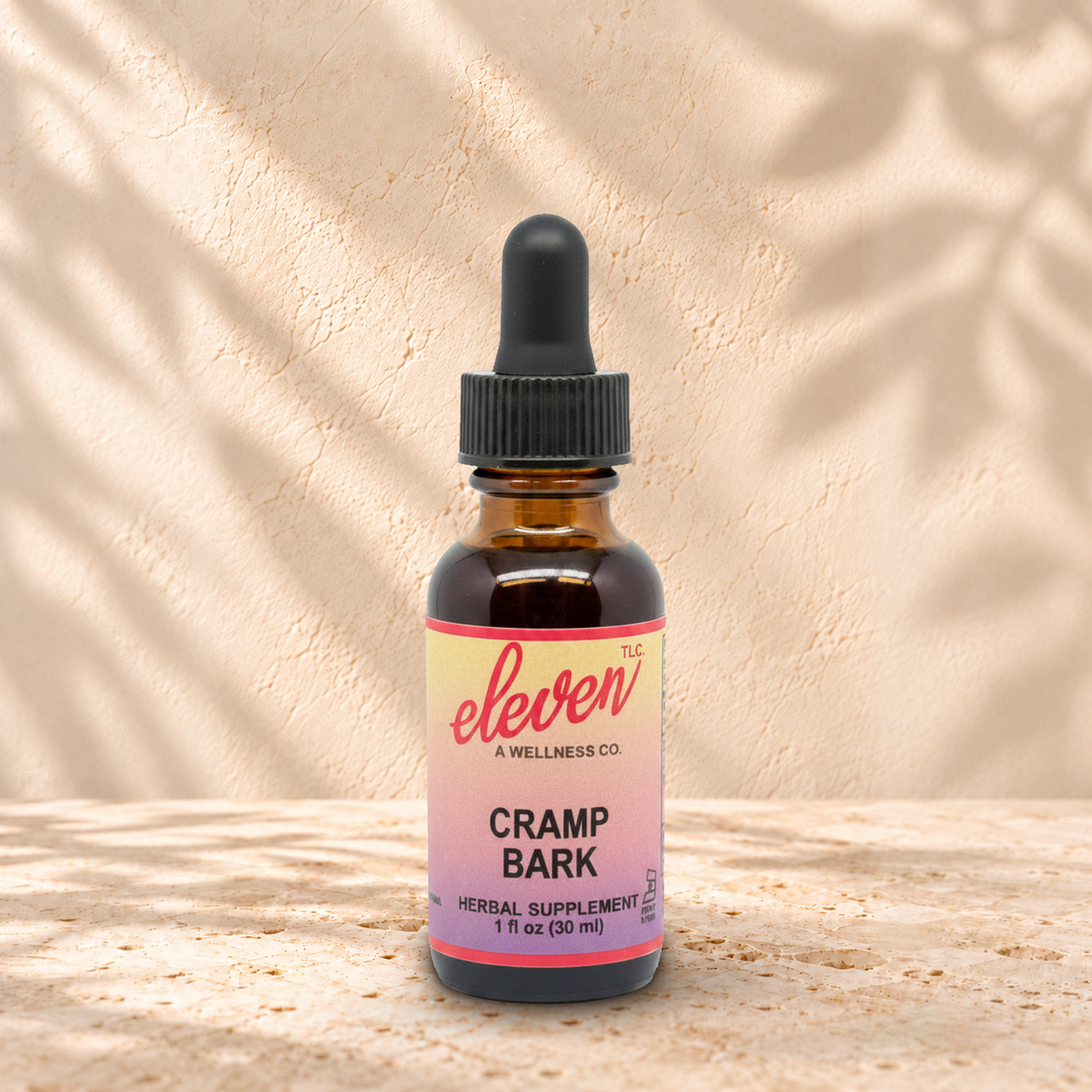Eleven TLC Cramp Bark 1 fl oz tincture in an amber glass bottle with a black dropper on warm travertine against a cream plaster wall.