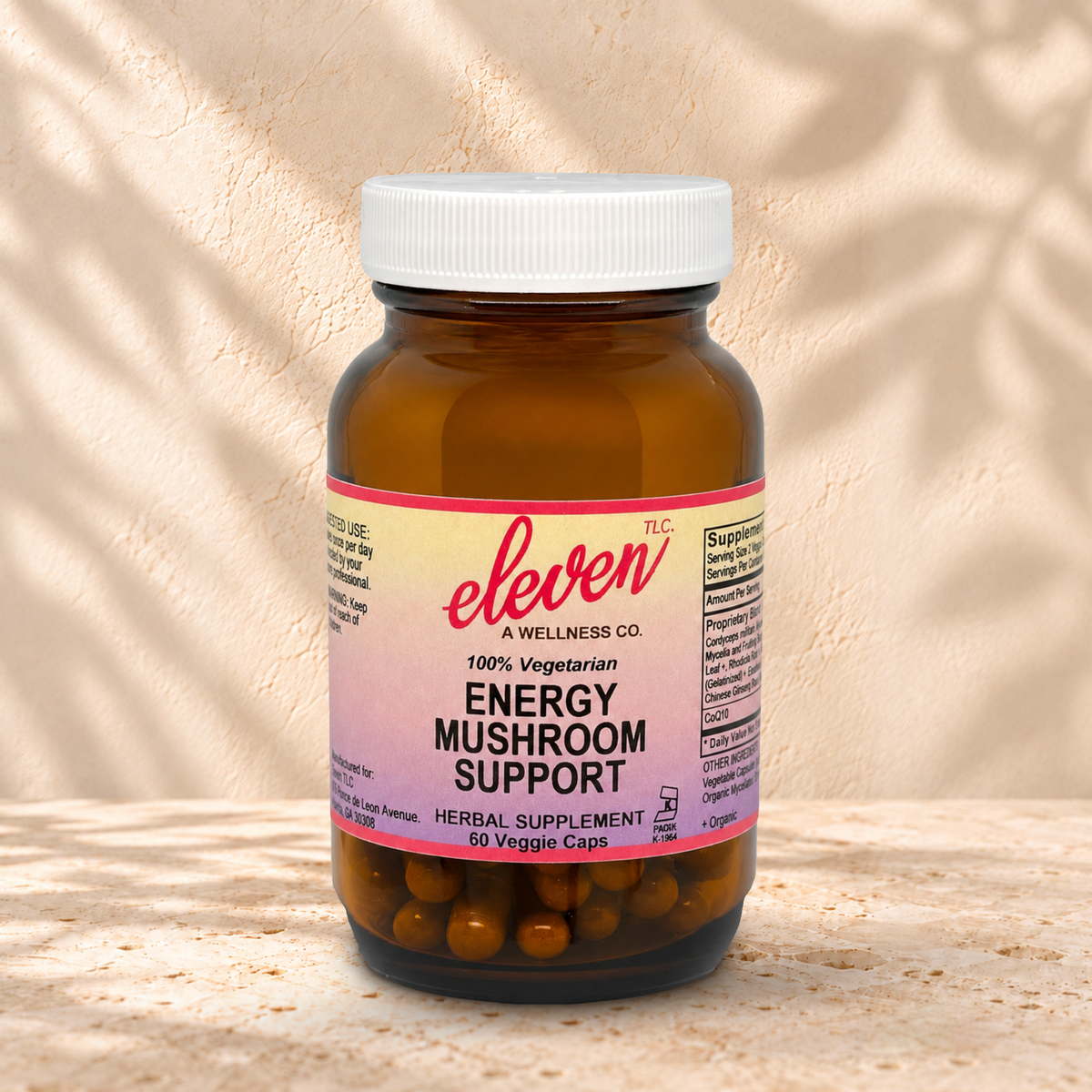 Eleven TLC Energy Mushroom 60-count capsule bottle with a white lid on warm travertine against cream plaster, with soft contact shadows.