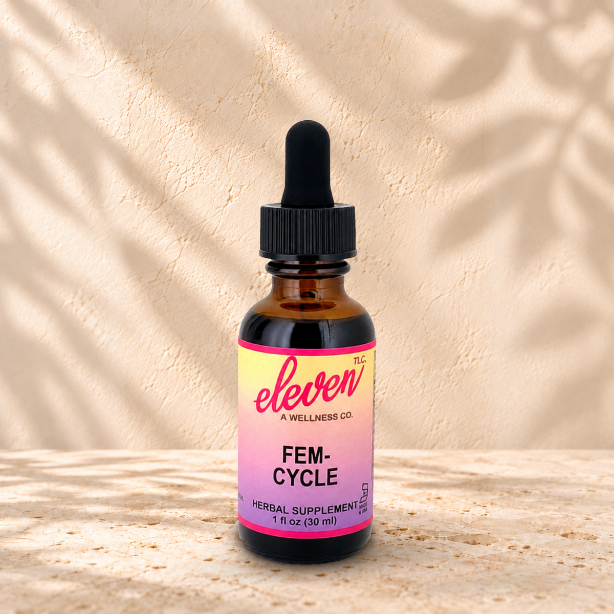 Eleven TLC Fem-Cycle 1 fl oz tincture in an amber glass bottle with a black dropper on warm travertine against a cream plaster wall.