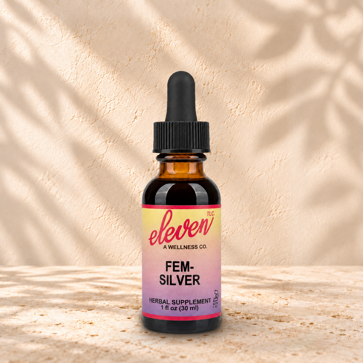 Eleven TLC Fem-Silver 1 fl oz tincture in an amber glass bottle with a black dropper on warm travertine against a cream plaster wall.