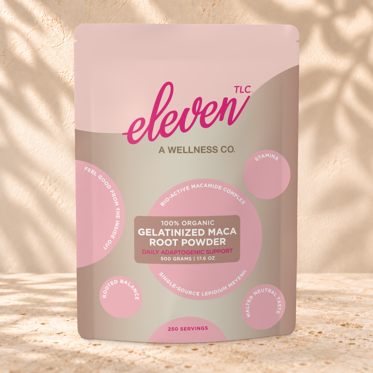 Front view of an Eleven TLC Gelatinized Maca Root Powder 500g pouch on warm travertine against a cream plaster wall with botanical shadows.