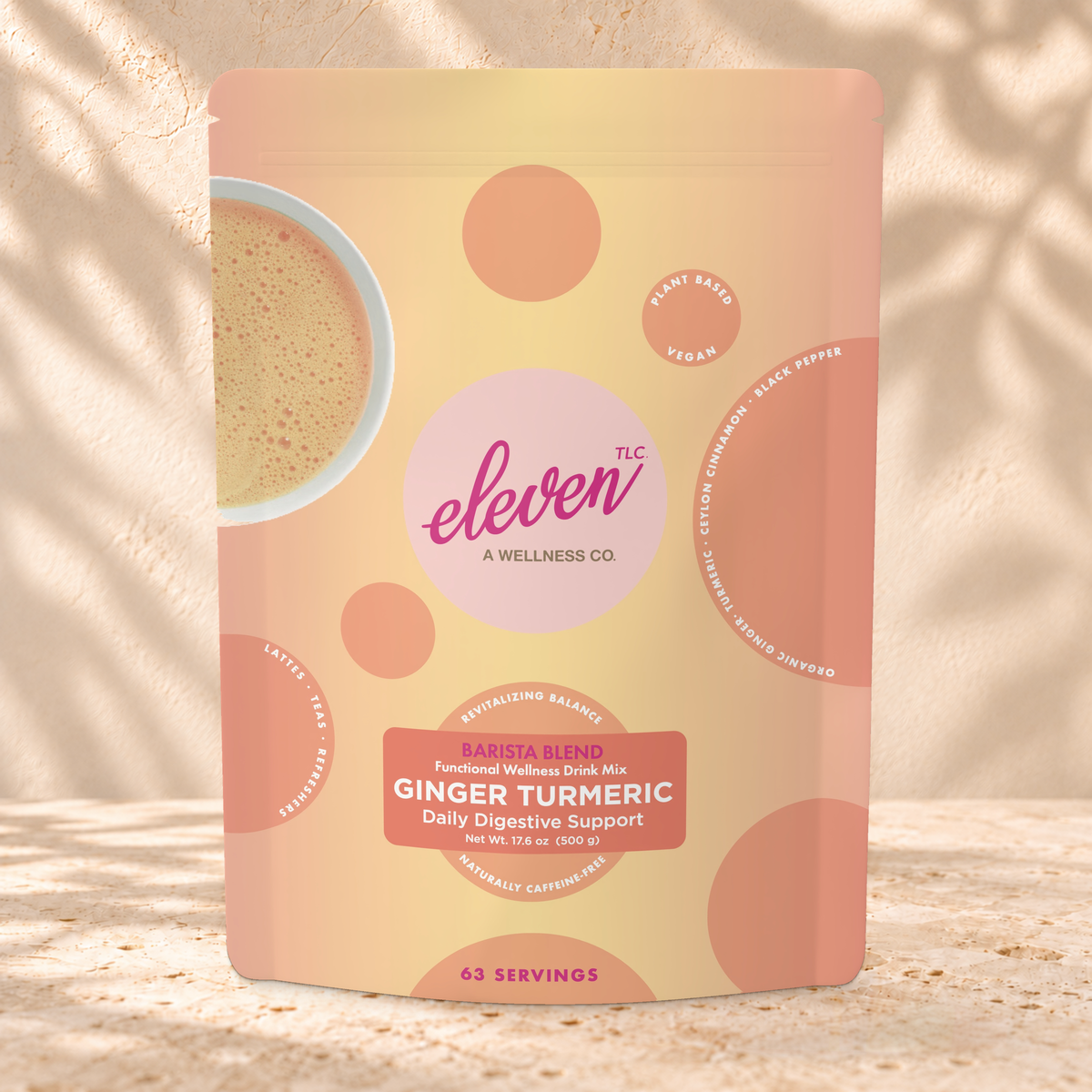 Front view of an Eleven TLC Ginger Turmeric 500g pouch on warm travertine against a cream plaster wall with botanical shadows.