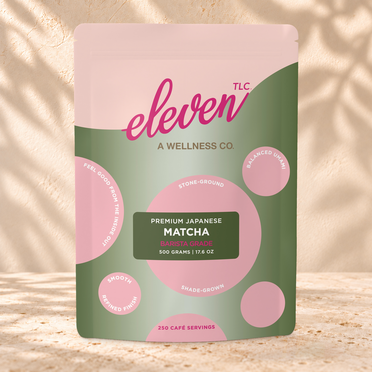 Front view of an Eleven TLC Japanese Matcha 500g pouch on warm travertine against a cream plaster wall with botanical shadows.