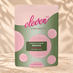 Front view of an Eleven TLC Japanese Matcha 500g pouch on warm travertine against a cream plaster wall with botanical shadows.