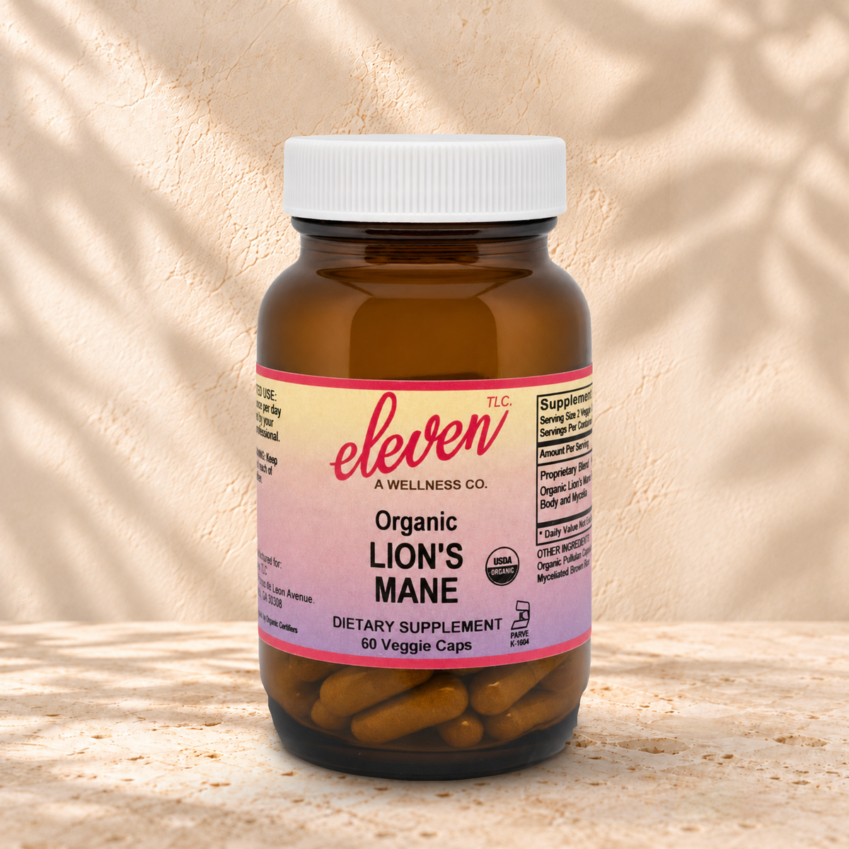 Eleven TLC Lion’s Mane 60-count capsule bottle with a white lid on warm travertine against cream plaster, with soft contact shadows.