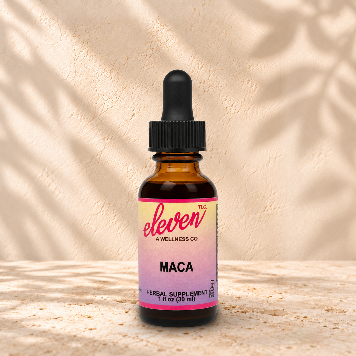 Eleven TLC Maca 1 fl oz tincture in an amber glass bottle with a black dropper on warm travertine against a cream plaster wall.