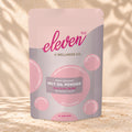 Front view of an Eleven TLC MCT Oil Powder 500g pouch on warm travertine against a cream plaster wall with botanical shadows.