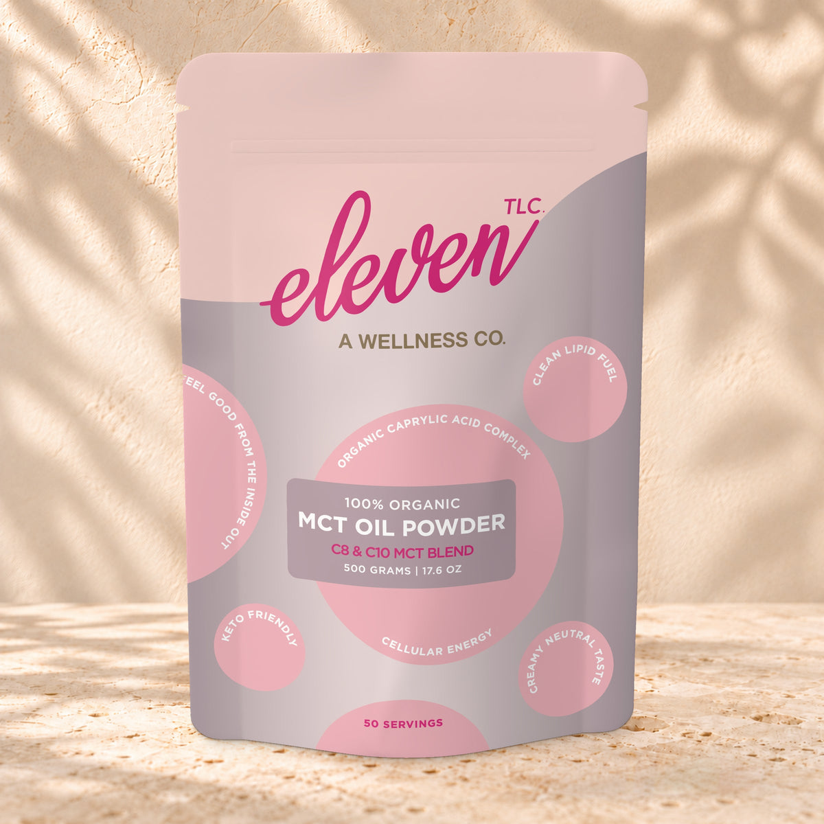 Front view of an Eleven TLC MCT Oil Powder 500g pouch on warm travertine against a cream plaster wall with botanical shadows.