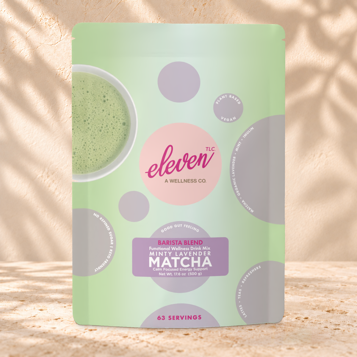 Front view of an Eleven TLC Minty Lavender Matcha 500g pouch on warm travertine against a cream plaster wall with botanical shadows.