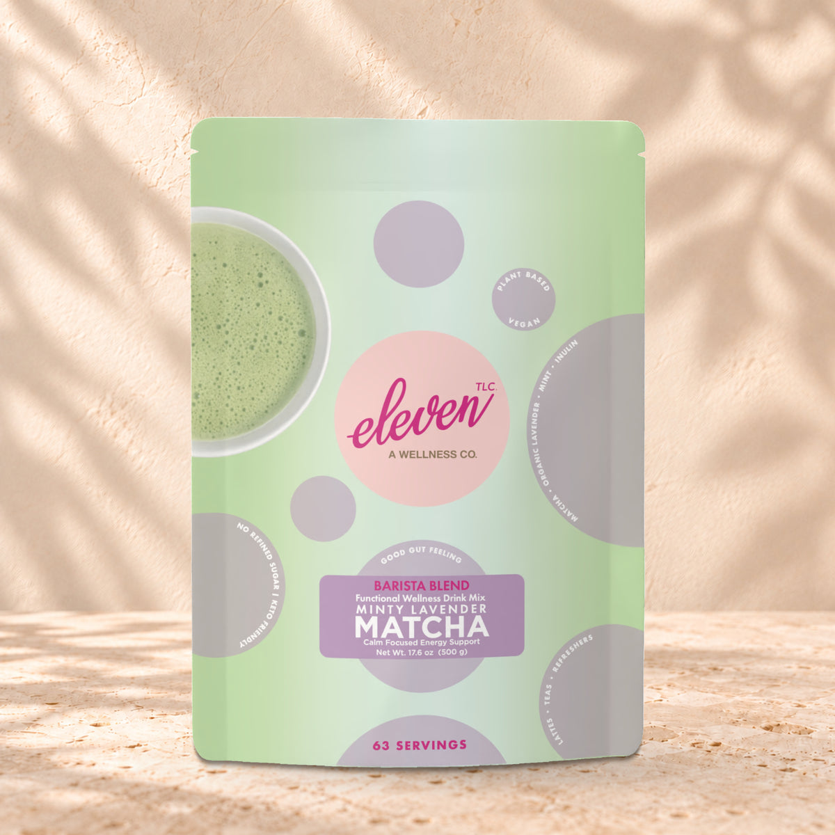 Eleven TLC Minty Lavender Matcha 500g stand-up pouch on travertine stone against a warm cream plaster wall, lit from the left with a soft shadow to the right.
