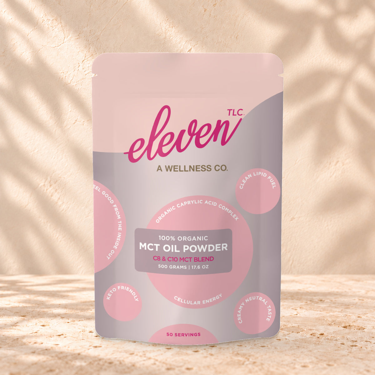 Eleven TLC Organic C8/C10 MCT Oil Powder 500g stand-up pouch on travertine stone against a warm cream plaster wall, lit from the left with a soft shadow to the right.