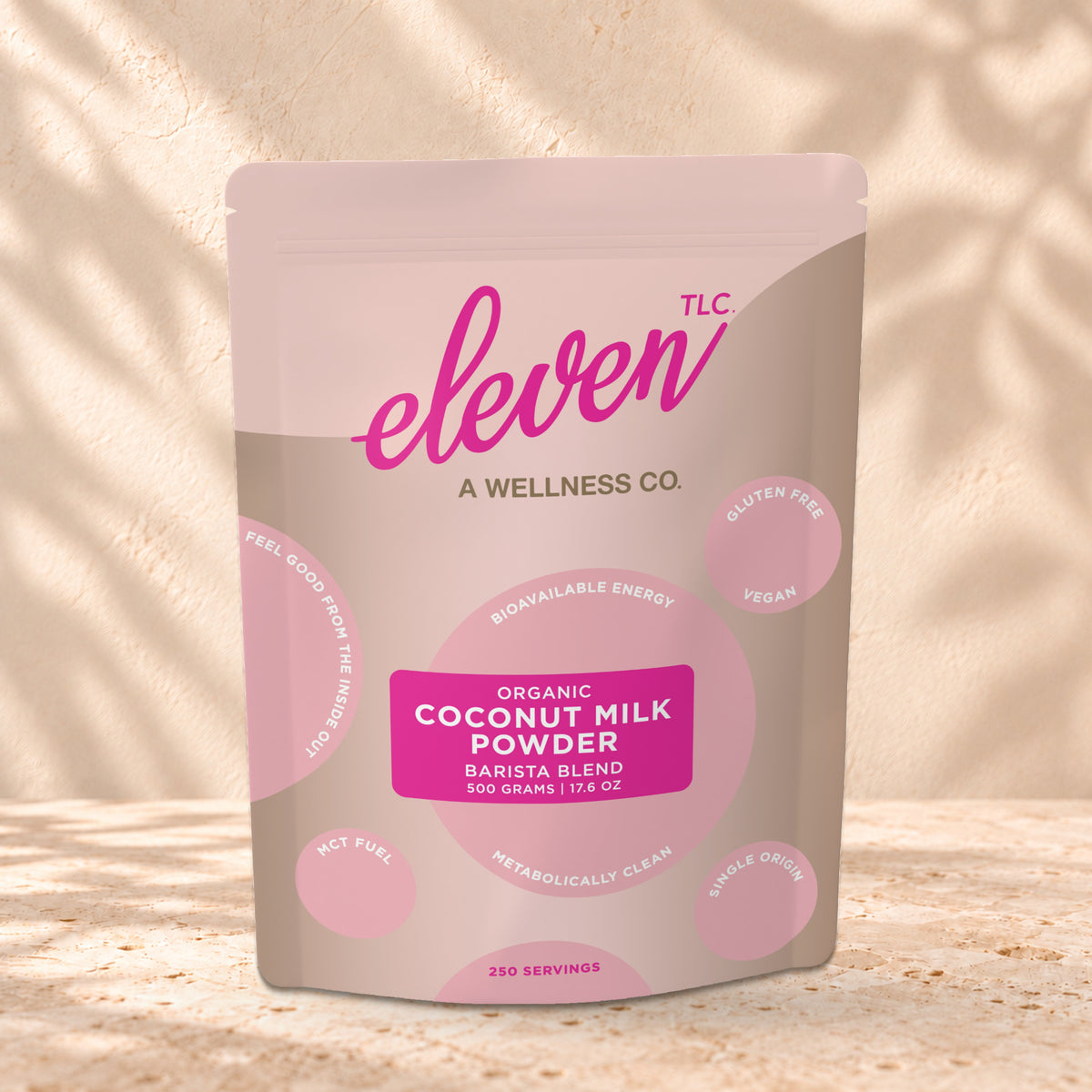 Eleven TLC Coconut Milk Powder 500g stand-up pouch on travertine stone against a warm cream plaster wall, lit from the left with a soft shadow to the right.