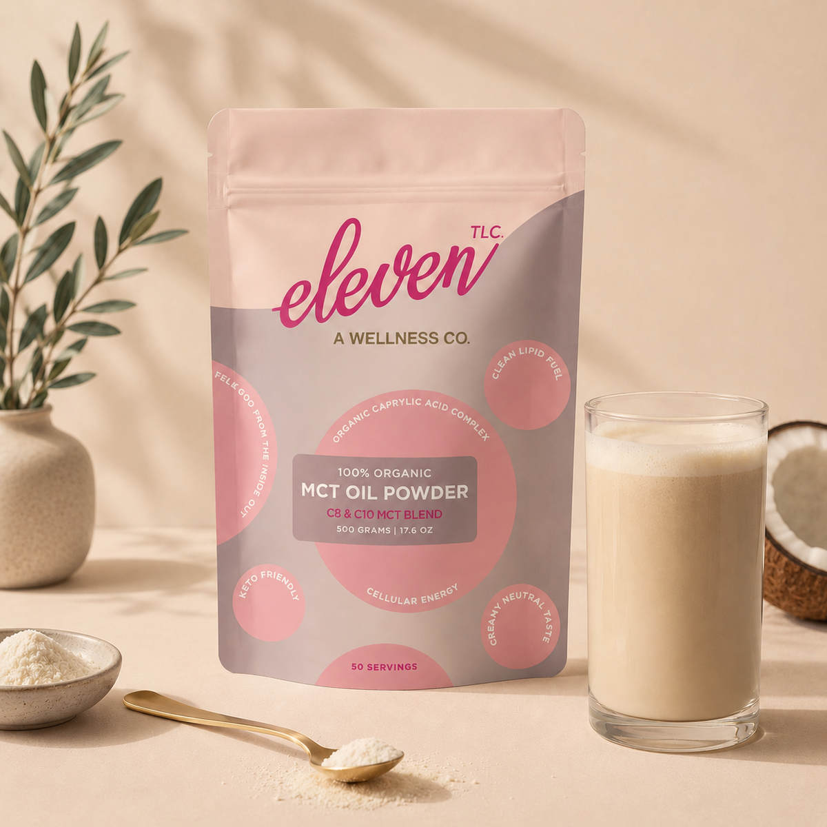 Eleven TLC organic MCT oil powder 500g pouch beside a glass of creamy milk, a bowl and gold spoon of white powder, coconut halves and an olive branch in warm light.